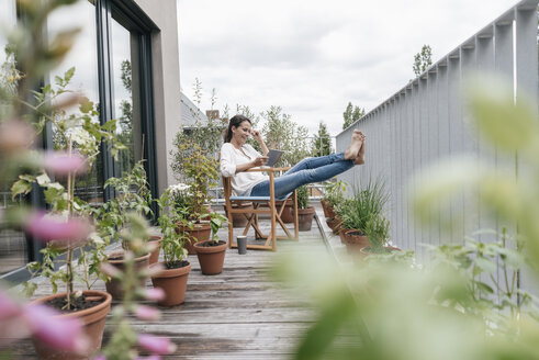 Lächelnde Frau entspannt sich auf dem Balkon und benutzt ein Tablet - JOSF01573
