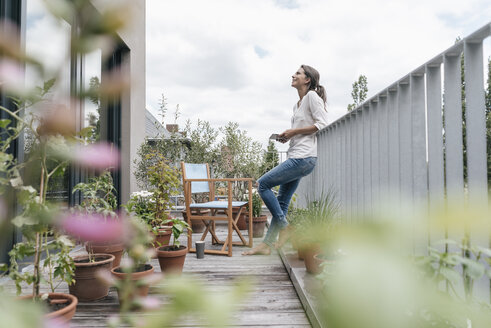 Smiling woman relaxing on balcony holding tablet - JOSF01575