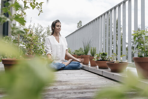 Woman sitting on balcony practicing yoga - JOSF01578