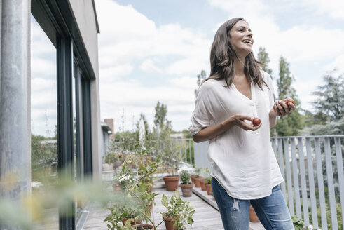 Glückliche Frau auf Balkon mit Tomaten in der Hand - JOSF01583