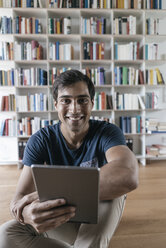 Portrait of smiling man at home holding tablet - JOSF01586
