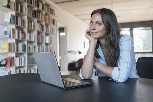 Porträt einer lächelnden Frau, die mit einem Laptop am Tisch sitzt - JOSF01608