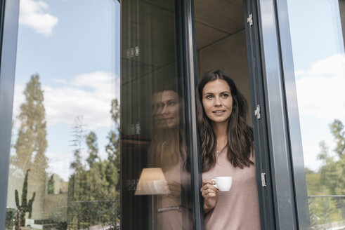 Lächelnde Frau, die eine Tasse hält und aus der Balkontür schaut - JOSF01613