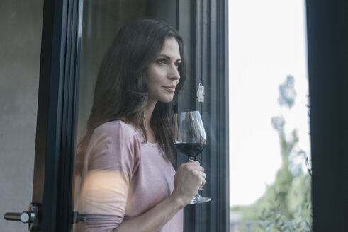 Lächelnde Frau hält ein Glas Rotwein und schaut aus dem Fenster - JOSF01615