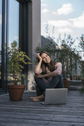 Smiling woman with laptop sitting on balcony - JOSF01621