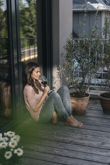 Frau mit Glas Rotwein entspannt auf Balkon - JOSF01624