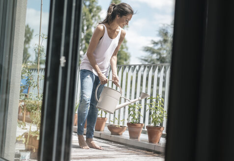 Smiling woman on balcony watering plants - JOSF01630
