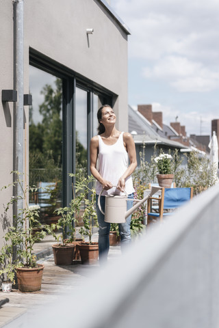 Smiling woman on balcony holding watering can stock photo