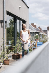 Smiling woman on balcony holding watering can - JOSF01631