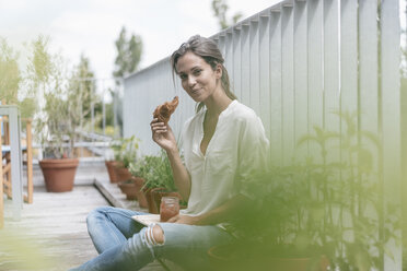 Smiling woman eating croissant with jam on balcony - JOSF01632