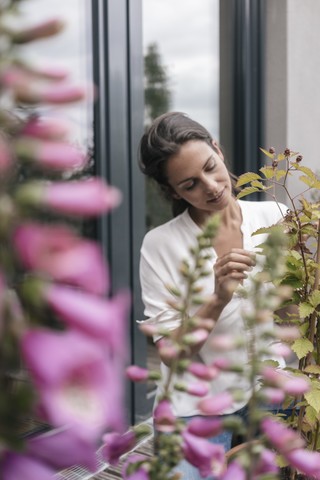 Frau kümmert sich um Pflanze auf Balkon, lizenzfreies Stockfoto