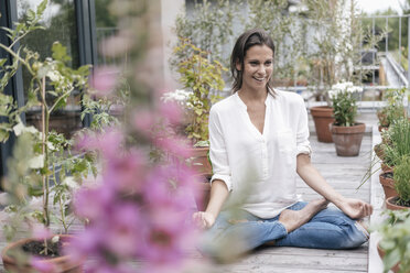 Happy woman sitting on balcony practicing yoga - JOSF01642