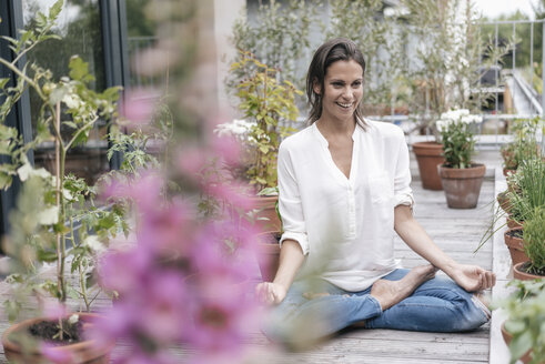 Glückliche Frau sitzt auf dem Balkon und übt Yoga - JOSF01642