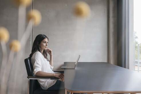 Nachdenkliche Frau sitzt am Tisch mit Laptop - JOSF01657