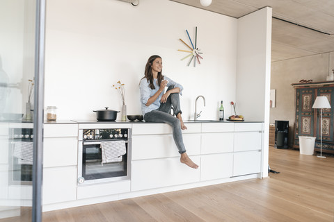 Lächelnde Frau entspannt sich in der Küche zu Hause, lizenzfreies Stockfoto