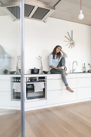 Lächelnde Frau entspannt sich in der Küche zu Hause, lizenzfreies Stockfoto