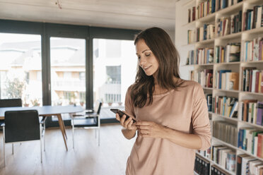 Smiling woman looking at cell phone at home - JOSF01685