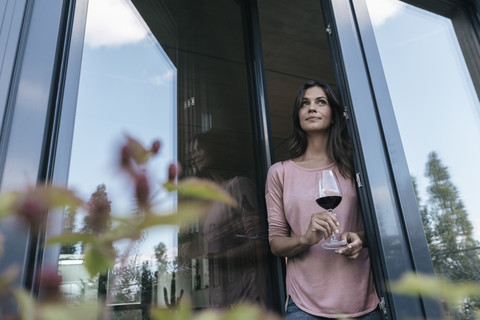 Frau hält ein Glas Rotwein und schaut aus dem Fenster, lizenzfreies Stockfoto