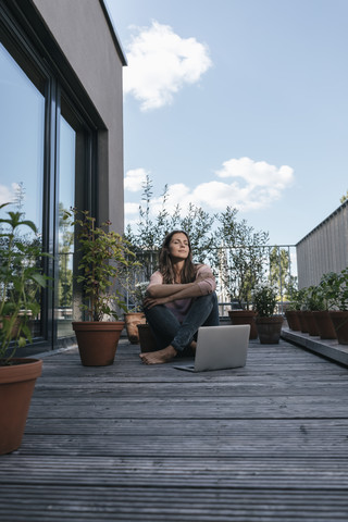 Frau mit Laptop auf dem Balkon sitzend, lizenzfreies Stockfoto