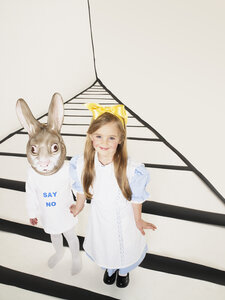 Porträt eines lächelnden kleinen Mädchens, verkleidet als Alice im Wunderland, Hand in Hand mit einem Mädchen mit Kaninchenmaske - FSF00955