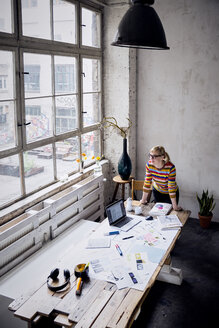 Woman standing at desk in a loft looking through window - RBF05954
