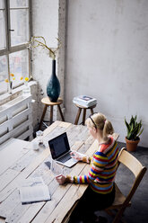 Woman sitting at desk in a loft using laptop and tablet - RBF05955