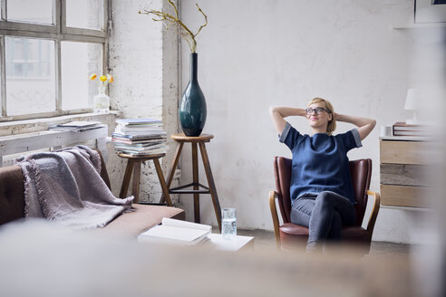 Lächelnde Frau sitzt auf einem Sessel in einem Loft und schaut durch ein Fenster - RBF05963