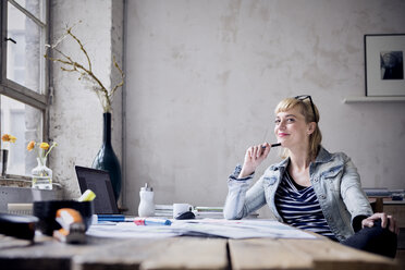 Portrait of smiling woman sitting at desk in a loft - RBF05972