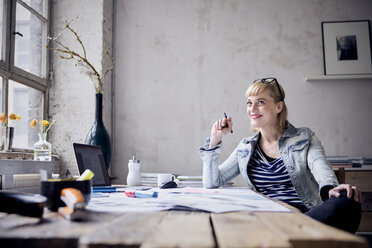 Portrait of laughing woman sitting at desk in a loft - RBF05974