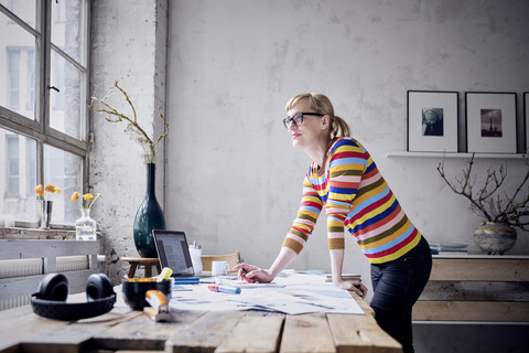 Portrait of smiling woman standing at desk in a loft looking through window stock photo