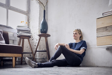 Smiling woman sitting on the floor in loft - RBF05994