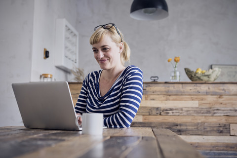 Porträt einer lächelnden Frau, die am Tisch sitzt und einen Laptop benutzt, lizenzfreies Stockfoto