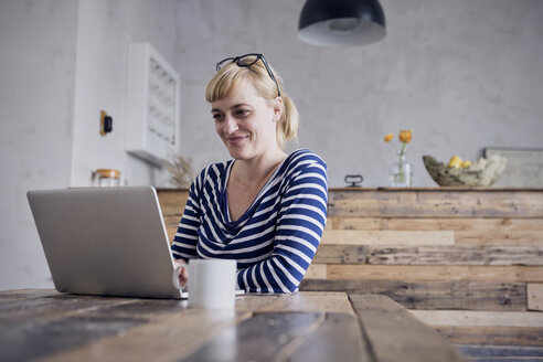 Porträt einer lächelnden Frau, die am Tisch sitzt und einen Laptop benutzt - RBF06000