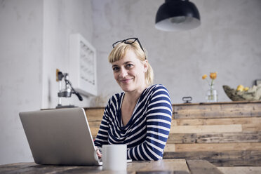Porträt einer lächelnden Frau, die mit Laptop und Kaffeetasse am Tisch sitzt - RBF06001