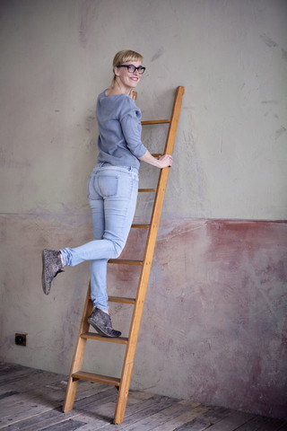 Lächelnde Frau, die auf einer Leiter in einem unrenovierten Raum eines Dachbodens steht, lizenzfreies Stockfoto