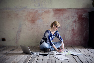 Frau sitzt auf Holzboden in einem unrenovierten Raum eines Dachbodens und arbeitet - RBF06014