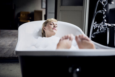 Blond woman taking bubble bath in a loft - RBF06018