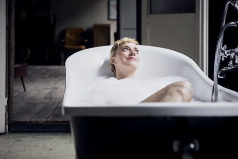 Portrait of happy woman taking bubble bath in a loft - RBF06019