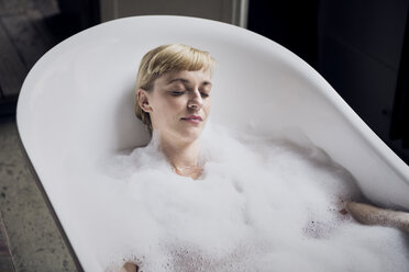 Portrait of woman with eyes closed taking bubble bath in a loft - RBF06023