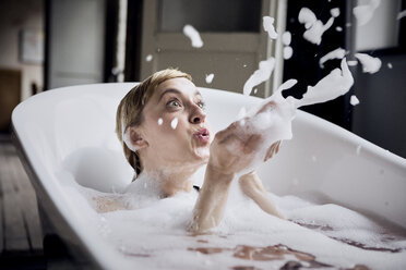 Blond woman taking bubble bath blowing foam in the air - RBF06026
