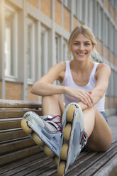 Smiling young inline-skater sitting on bench - JUNF00895