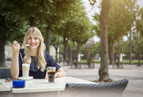 Porträt einer lachenden blonden Frau, die in einem Straßencafé sitzt, lizenzfreies Stockfoto