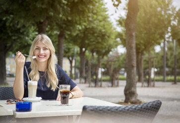 Porträt einer lachenden blonden Frau, die in einem Straßencafé sitzt - JUNF00903