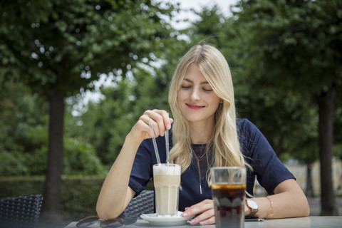 Porträt einer blonden Frau, die mit einem Latte Macchiato in einem Straßencafé sitzt, lizenzfreies Stockfoto