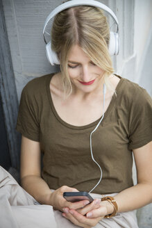 Relaxed young woman listening music with headphones and cell phone - JUNF00912