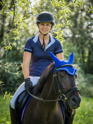 Lächelnde junge Frau reitet auf einem Feld - STSF01311