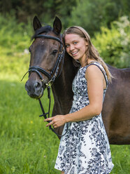 Lächelnde junge Frau und Pferd auf einer Wiese - STSF01312