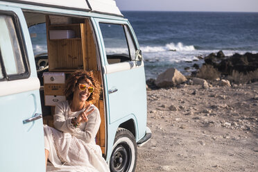 Spanien, Teneriffa, lachende Frau, die in einem am Meer geparkten Lieferwagen sitzt und das Siegeszeichen zeigt - SIPF01720