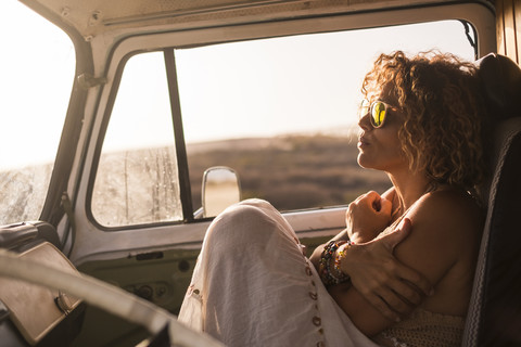 Nachdenkliche Frau, die bei Sonnenuntergang in einem geparkten Auto sitzt, lizenzfreies Stockfoto