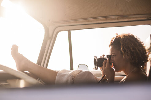 Frau sitzt in geparktem Van und fotografiert bei Sonnenuntergang - SIPF01726